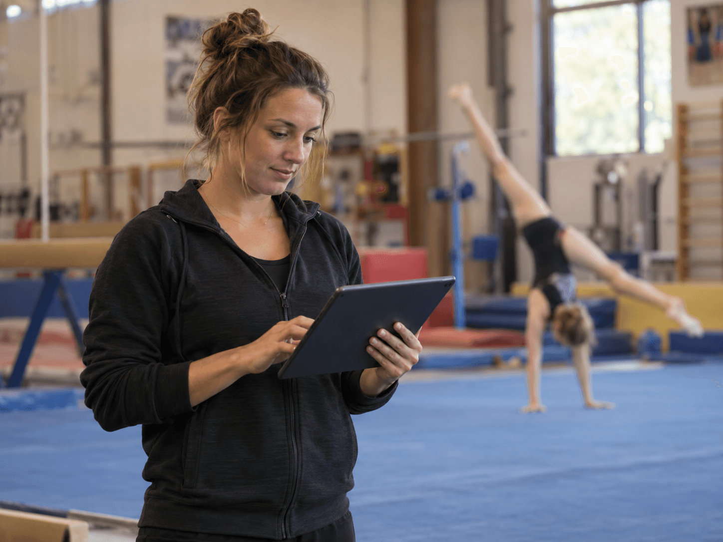 A gymnastics coach reviewing training notes on a tablet